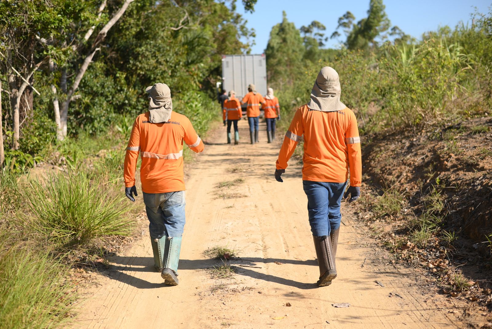 Equipe de campo caminha por uma estrada de terra a caminho das visitas
